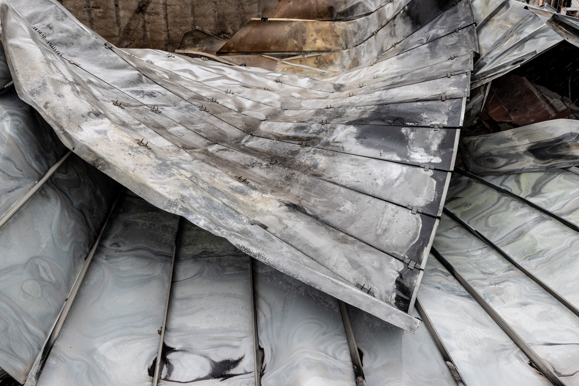 A zinc metal roof warped and folded by the heat of the Palisades Fire