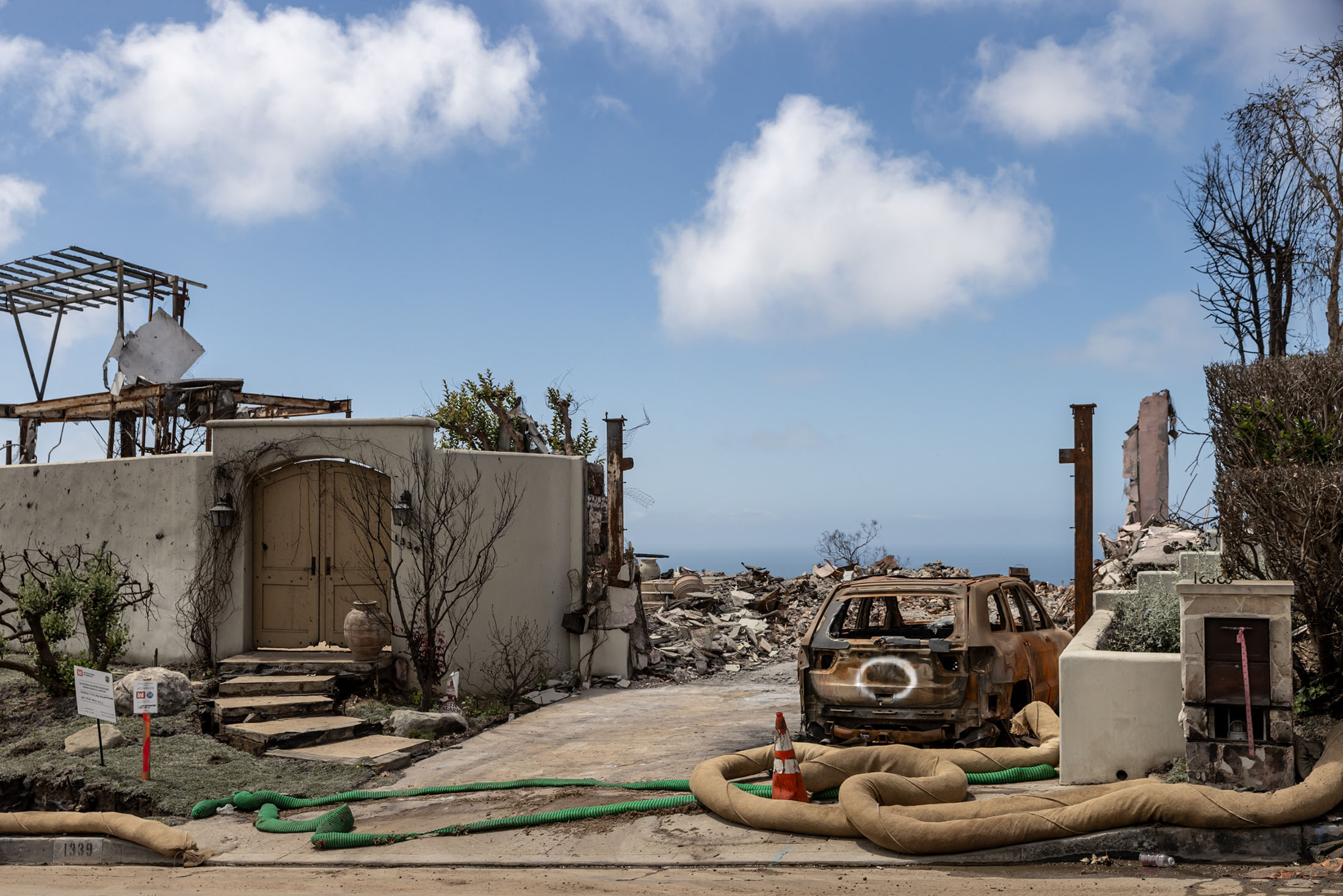 Street view of a house destroyed by the Palisades Fire with a marked vehicle in the driveway